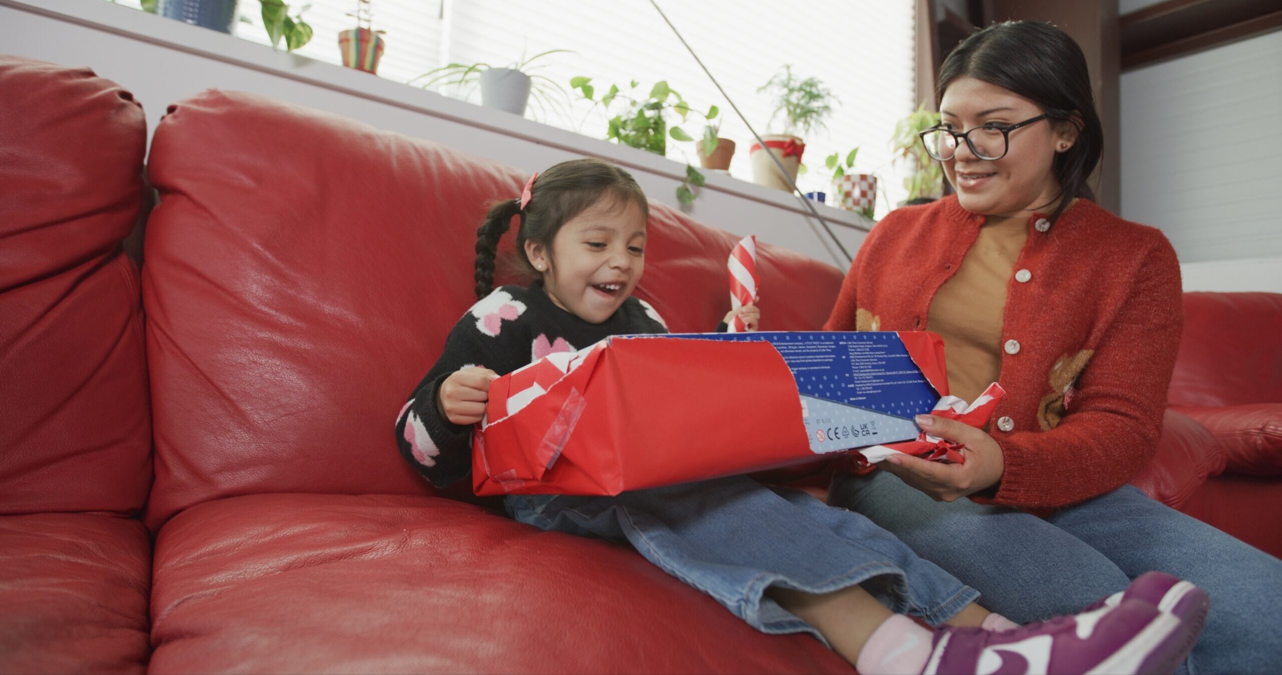 Child sitting on a couch with her parent, opening a Christmas present from the Precious Gift drive at A Precious Child